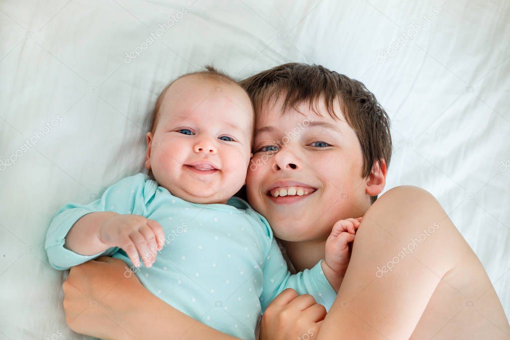 Cute boy and newborn baby girl. Toddler kid hugging his sibling.