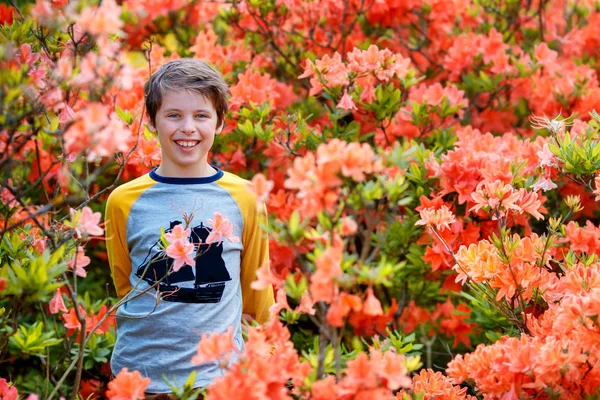 Spring portrait of cute attractive 10 year old boy posing in the garden next to blossoming pink Rhododendron — Stock Photo, Image