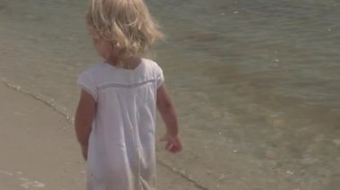 Güzel küçük bir kız deniz kıyısı yürür. Deniz kenarı beyaz elbiseli küçük kız. Ağır çekim.