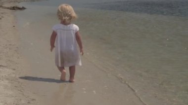 Bebek çalıştırıyor. Küçük bir kız yavaş kıyı boyunca çalışır. Tropikal deniz kıyısında ağır çekimde kız çocuk. Deniz kenarında tatil yaz.