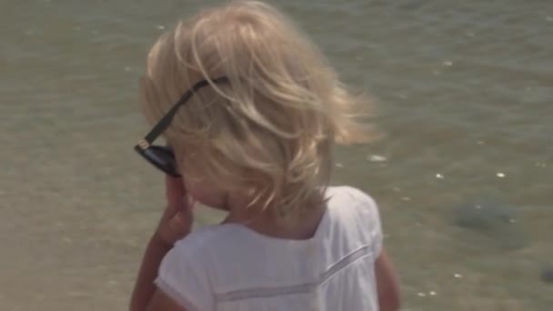 Kleines Mädchen mit Sonnenbrille an der Küste. — Stockvideo