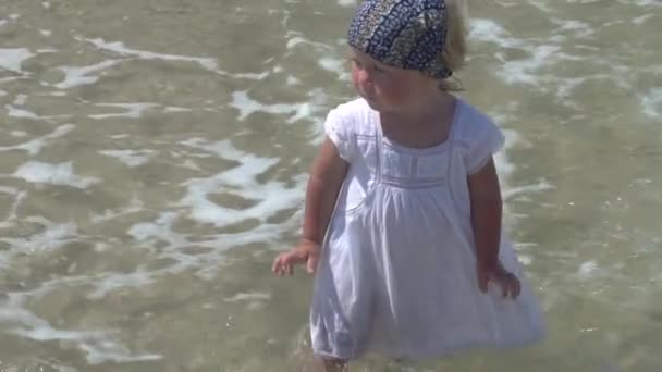 Un niño está parado en el agua del mar. Niña con un vestido blanco camina en el agua del mar . — Vídeos de Stock