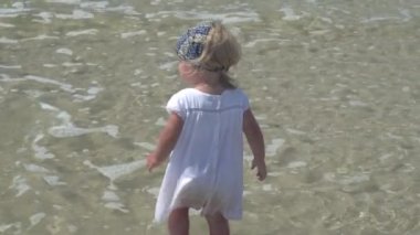 Bir çocuk deniz suyu içinde duruyor. Beyaz elbiseli küçük kız deniz suda yürüyor.