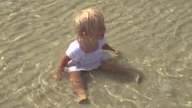 Çocuk denizde oturur. Küçük kız sahilde su oturan.