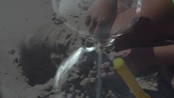 Reloj de arena de vidrio en el fondo de un niño jugando. Un niño construye un castillo de arena. — Vídeos de Stock