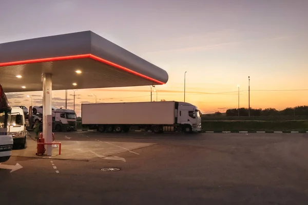 Benzin İstasyonu ve beyaz kamyon üzerinde günbatımı ve erken sabah saatte ayakta araçları ile yakıt ikmali yan görünüm. Gece gündüz iş kavramı. Boş kopya alanı metin için.
