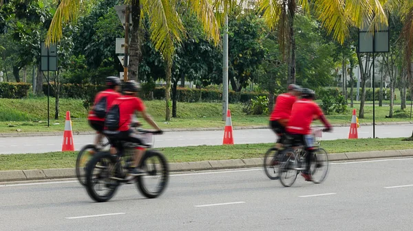 Group of bikers  ride along city road, four men on bicycles ride down street with palm trees. Photo with blur in motion. Malaysia, Cyberjaya.