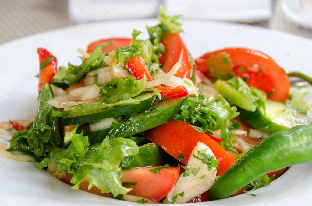 Healthy natural food, fresh salad with vegetables in plate - cucumbers, tomato, greens, close up. Shallow depth of field. Concept of vegetarianism, low calorie diet, weight loss, proper nutrition