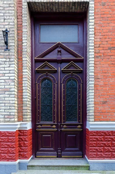 Front door, double purple doors with geometric elements, and glass. Brick wall.