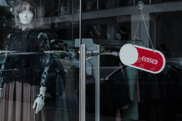 Glassdoor of a clothing store with a Closed  sign. Female mannequin on the shop window. Concept of an era of consumption, abundance, the end of discounts.