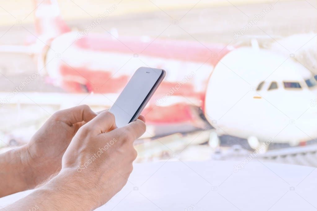 Close-up, male hands holding a mobile phone,  airport blurry  background.