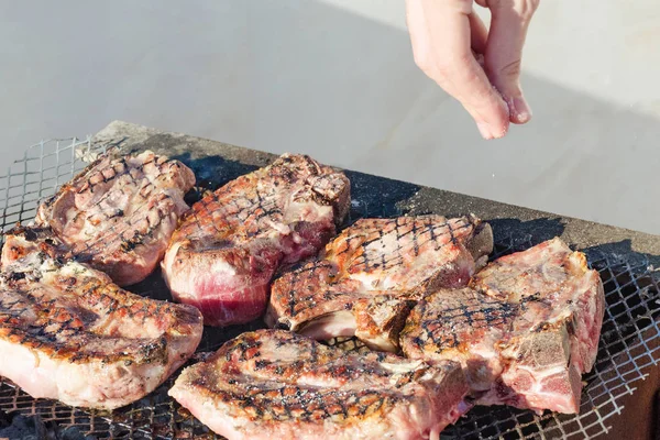 Cooks hand salt steaks in a barbecue.