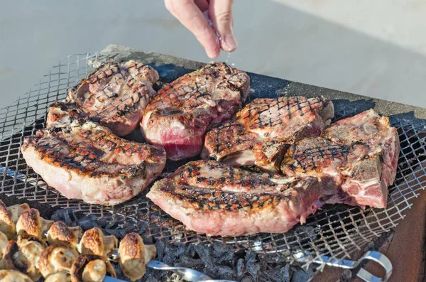 Cooks hand salt the meat on the grill. — Stock Photo, Image