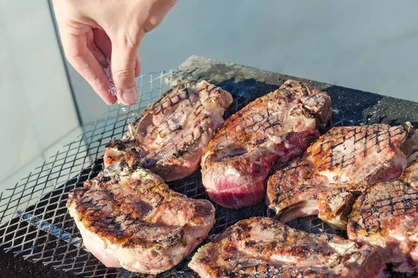 Cooks hand salt the meat in a barbecue.