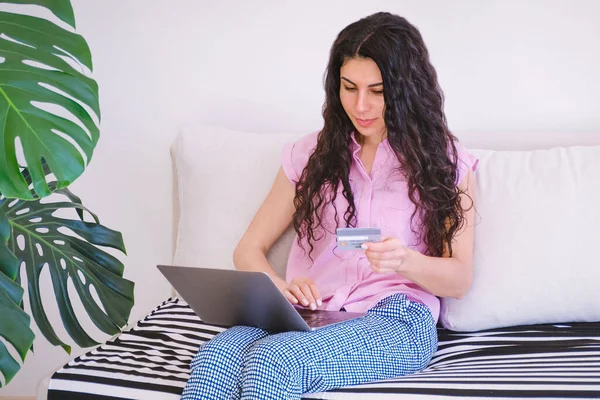Woman pays online by card from home with a laptop sitting on a sofa.  Remote secure payments
