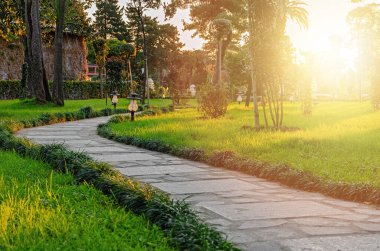 Gün batımında yeşil çimlerin ve ağaçların arasında kıvrılan bahçe taşı geçidi. Şehir parkında peyzaj. Batumi, Georgia.
