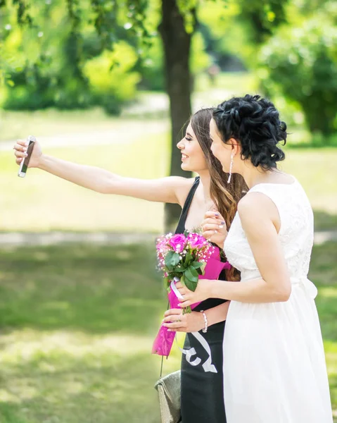 Portret dwóch przyjaciół młode ładne kobiety, biorąc selfie w lato zielony park. Ładny samice Panna młoda i druhna biorąc zdjęcie siebie z smartphone lub kamery na serwisie społecznościowym. — Zdjęcie stockowe