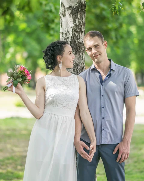 Portrait de belle jeune mariée de couple féminin avec petit bouquet de roses de fleurs de mariage et marié masculin tenant la main, souriant et se regardant dans le parc d'été — Photo