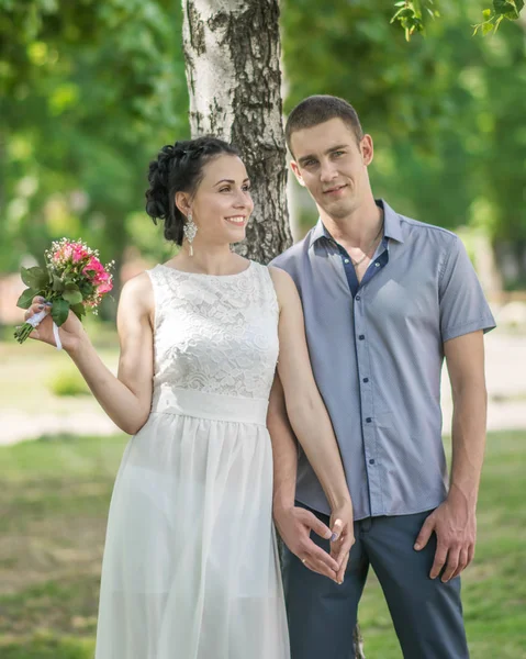 Portrait de belle jeune mariée de couple féminin avec petit bouquet de roses de fleurs de mariage et marié mâle debout et tenant la main, souriant dans le parc d'été — Photo