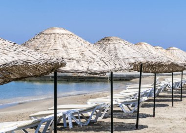 Güneşli bir yaz sabahı plajda şezlong ve şemsiyeler. Mavi deniz ve gökyüzü ile arka plan