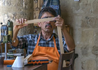 Kıbrıs, Lefkoşa - 10 Haziran 2019: Yerel sanat galerisinde oturan ve çalışan 60-75 yaşındaki yaşlı adamın portresi. İşyerinde elektrikli takım tezgahı üzerinde çalışan doğrama