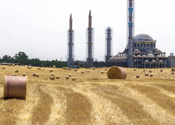 Hermoso paisaje en la isla de Chipre. Muchos fardos redondos de paja para alimentación animal sobre el fondo de la mezquita en construcción . —  Fotos de Stock