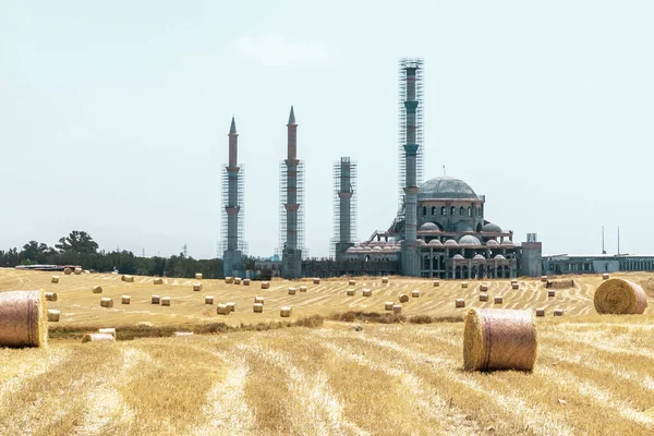 Güzel Kıbrıs Yaz Manzara. Yapımı devam eden gökyüzü ve Cami arka plana karşı hayvan yemi için yuvarlak saman balyaları ile alan. — Stok fotoğraf