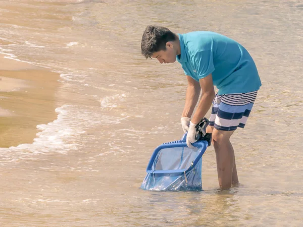 CYPRUS, KARAVAS, ALSANCAK - JUNHO 10, 2019: Jovem trabalhador que limpa a costa de detritos e resíduos. Homem trabalhando usando ferramentas — Fotografia de Stock