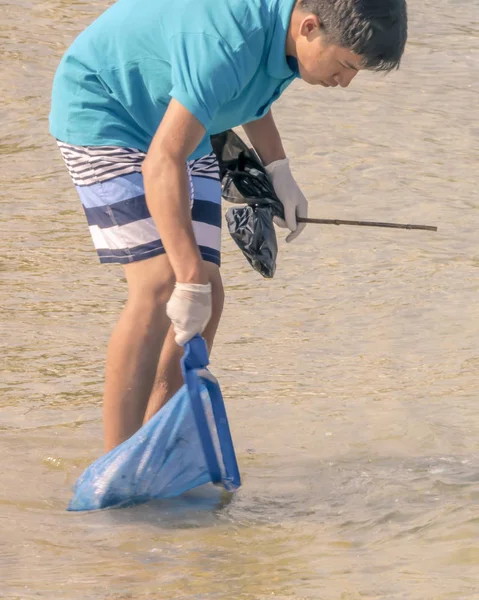 CHIPRE, KARAVAS, ALSANCAK - 10 DE JUNIO DE 2019: Niño limpiando la costa de escombros y desechos. asiático hombre trabajando usando herramientas — Foto de Stock