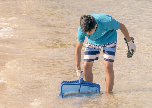 CHIPRE, KARAVAS, ALSANCAK - 10 DE JUNIO DE 2019: Niño limpiando la costa de la basura. El hombre que trabaja junto al mar usando herramientas — Foto de Stock