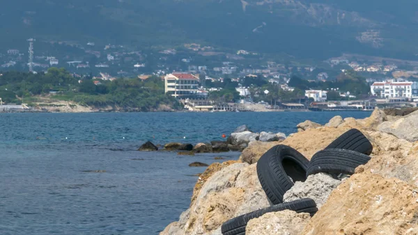 CYPRUS, KARAVAS, ALSANCAK - JUNE 10, 2019: Landscape with old car rubber tires on the rocks on seaside of the local beach. Environmental pollution concept — Stock Photo, Image