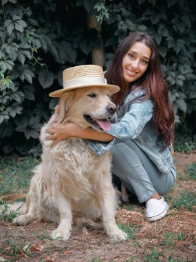 Genç güzel 30 yaşındaki kadın portresi onun evcil köpek Golden retriever açık bir şapka giyen ile oturan.