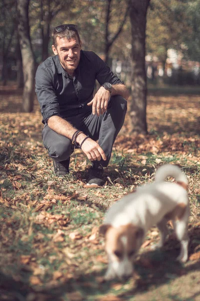 Портрет молодого счастливого человека и милого чистокровного собачника Джека Рассела-терьера, играющего вместе в осеннем городском парке. — стоковое фото