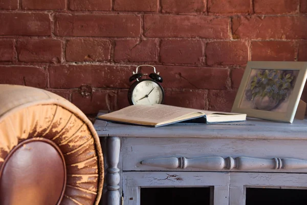 Desk clock with a book on a wooden cupboard against a brick wall background.