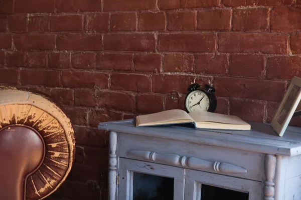 Desk clock with a book on a wooden cupboard against a brick wall background.