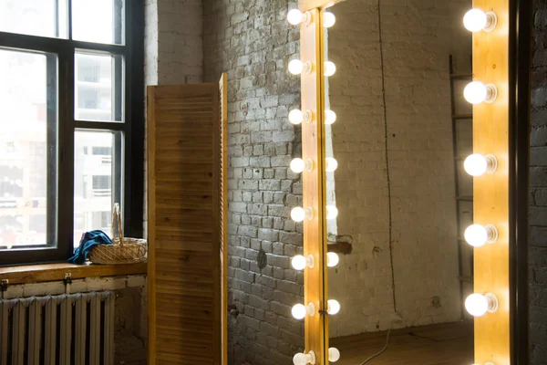 Large full-length mirror in a room with a brick wall and a window.