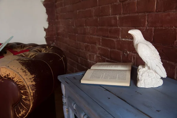 一只老鹰的雕像与一张打开的书和一个老扶手椅反对砖墙背景 — 图库照片