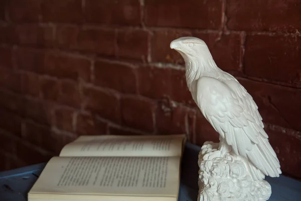一只老鹰的雕像与一张打开的书木桌在砖墙背景上 — 图库照片