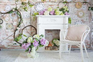 Bir şömine ve duvardaki bir saat ile bir odası iç tasarım. Bir Vazoda Çiçekler ile hasır sandalye