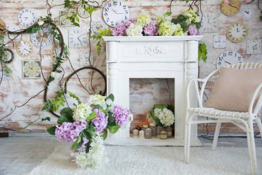 Bir şömine ve duvardaki bir saat ile bir odası iç tasarım. Bir Vazoda Çiçekler ile hasır sandalye