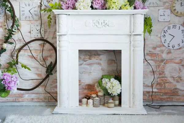 White decorative fireplace with flowers and candles. Background wall with clock and roses