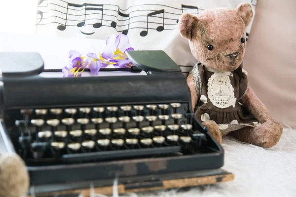 Старая черная пишущая машинка с плюшевым мишкой на фоне подушки с нотами — стоковое фото
