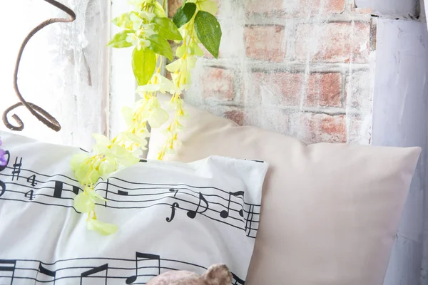 Kussen met muzieknoten op de vensterbank met bloemen. Baksteen muur achtergrond met kunstbloemen — Stockfoto