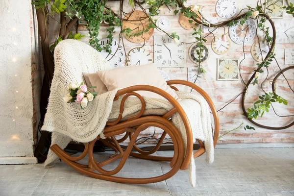 Фон с креслом-качалкой с подушками на фоне веток с цветами и настенными часами — стоковое фото