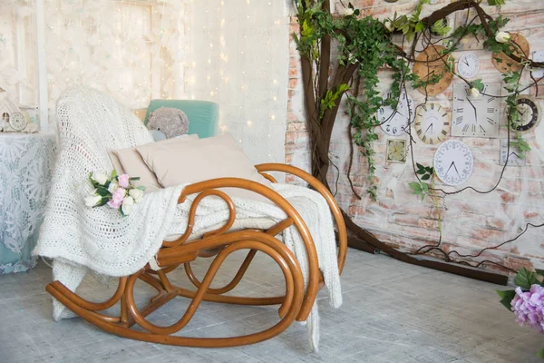 Background with rocking chair with pillows on the background of branches with flowers and wall clocks — Stock Photo, Image
