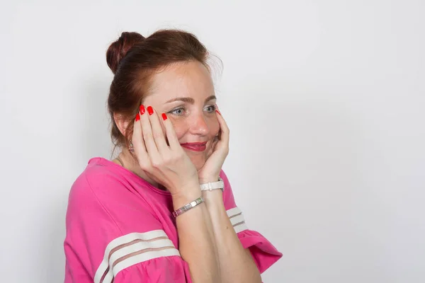 Gros plan d'une femme aux cheveux roux souriante avec les mains sur les joues regardant loin isolé sur fond blanc . — Photo