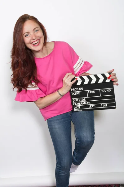 Mulher ruiva sorridente no topo rosa com placa de filme isolada — Fotografia de Stock