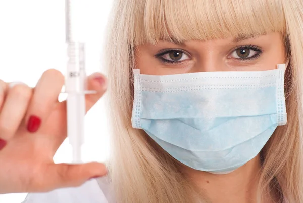 Close-up van een jonge blonde verpleegster in een masker met een spuit. — Stockfoto