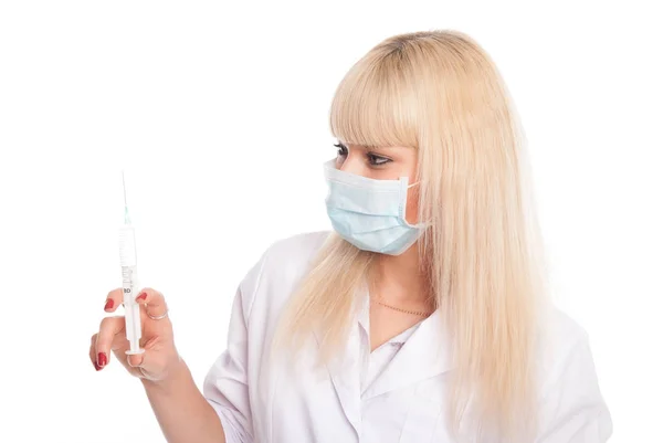 Close-up of a young blonde nurse in a mask looking at a syringe. — Stock Photo, Image