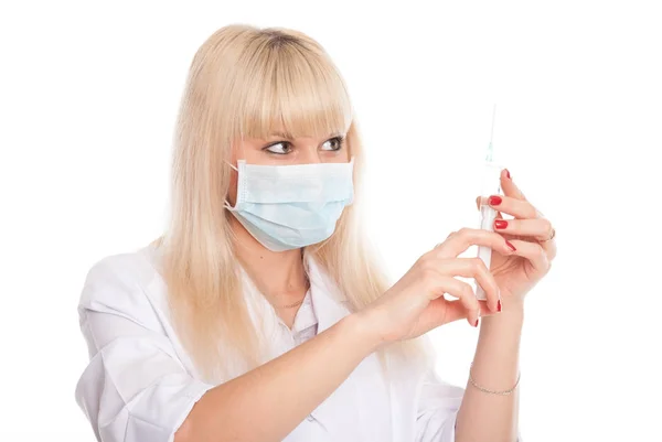 Close-up of a young blonde nurse in a mask looking at a syringe. — Stock Photo, Image